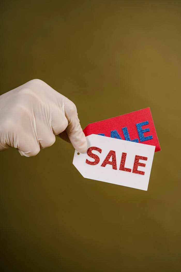 mobile-02 Gloved hand holding red and white sale tags on a green background, emphasizing shopping and discounts.